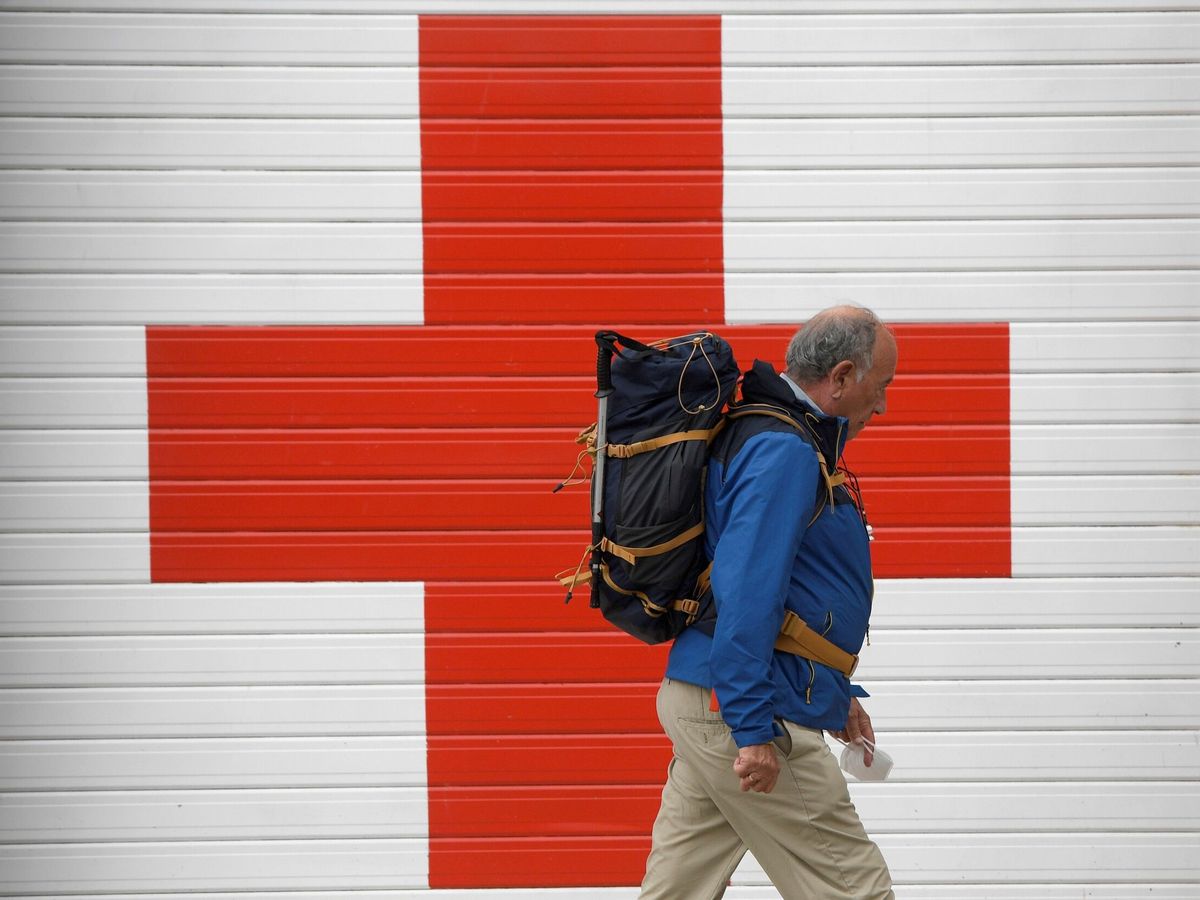 Foto:  Un hombre camina con la mascarilla en la mano ante la puerta de entrada de ambulancias del Hospital de la Cruz Roja, en Oviedo. (EFE/Eloy Alonso)