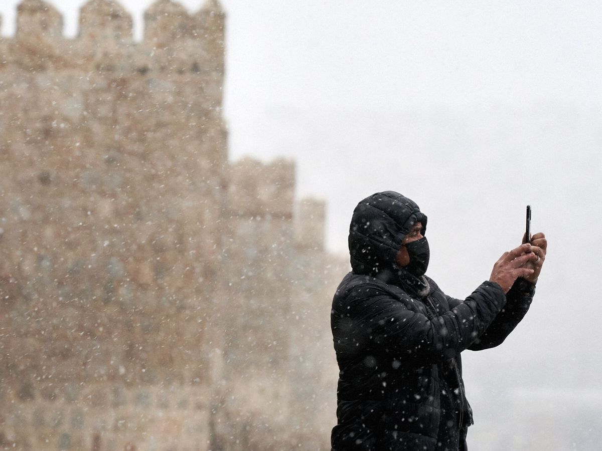 Foto: Un hombre se hace una foto con su teléfono móvil junto a la muralla de Ávila durante la primera nevada del otoño en la capital abulense. (Raúl Sanchidrián/EFE)
