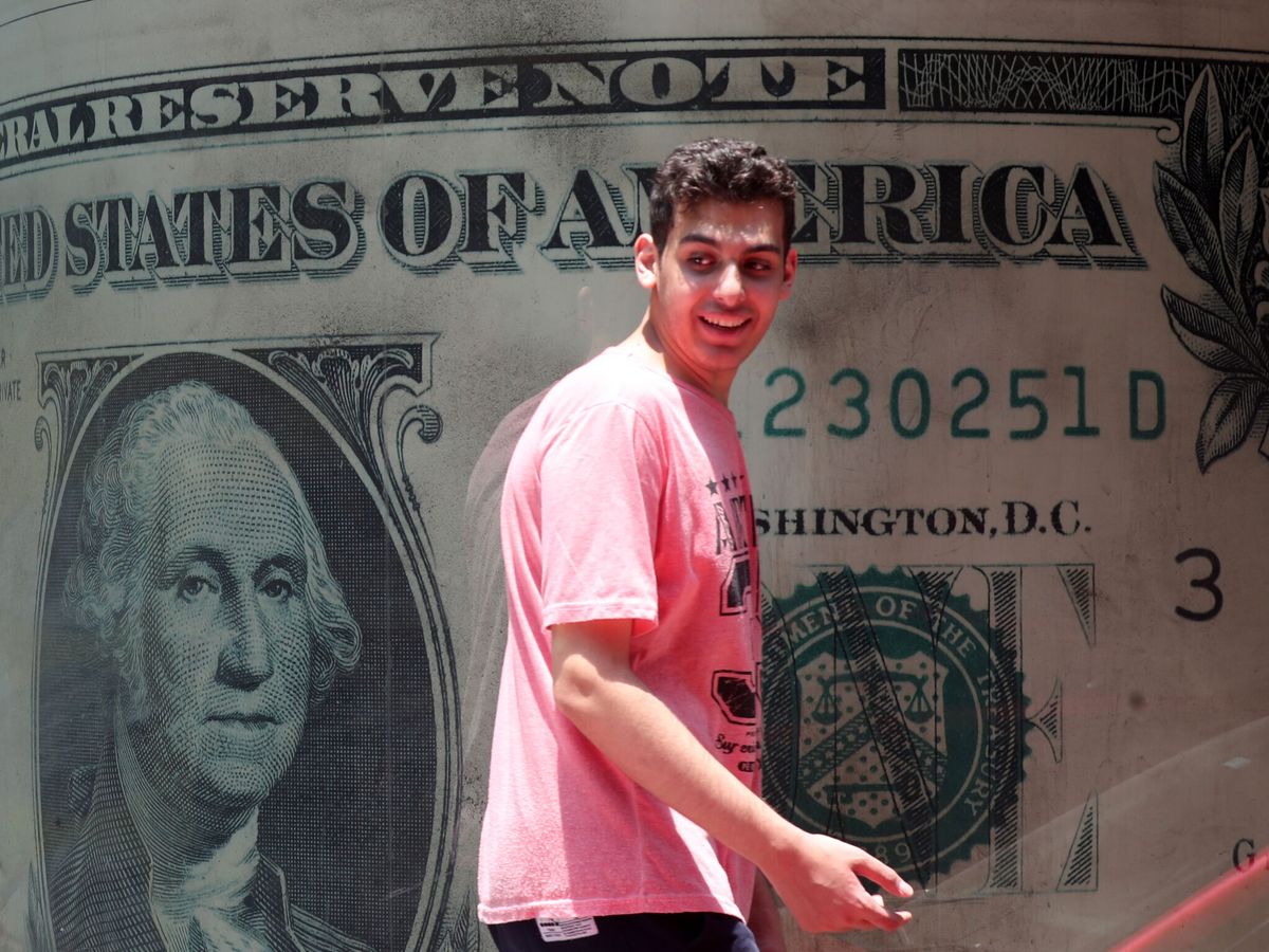 Foto: Un hombre camina junto a una imagen de un dólar. (EFE/Khaled Elfiqi)