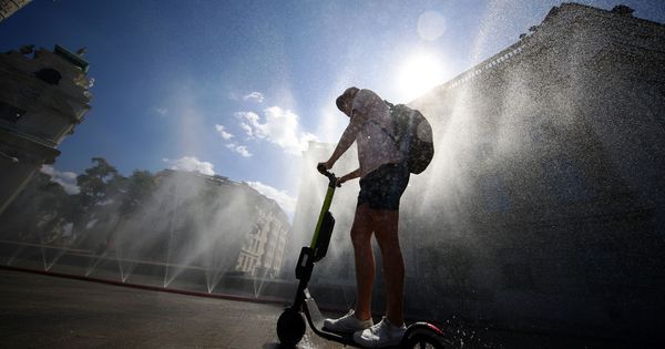 Foto: A man rides an electric scooter under water sprinklers during a heat wave in vienna