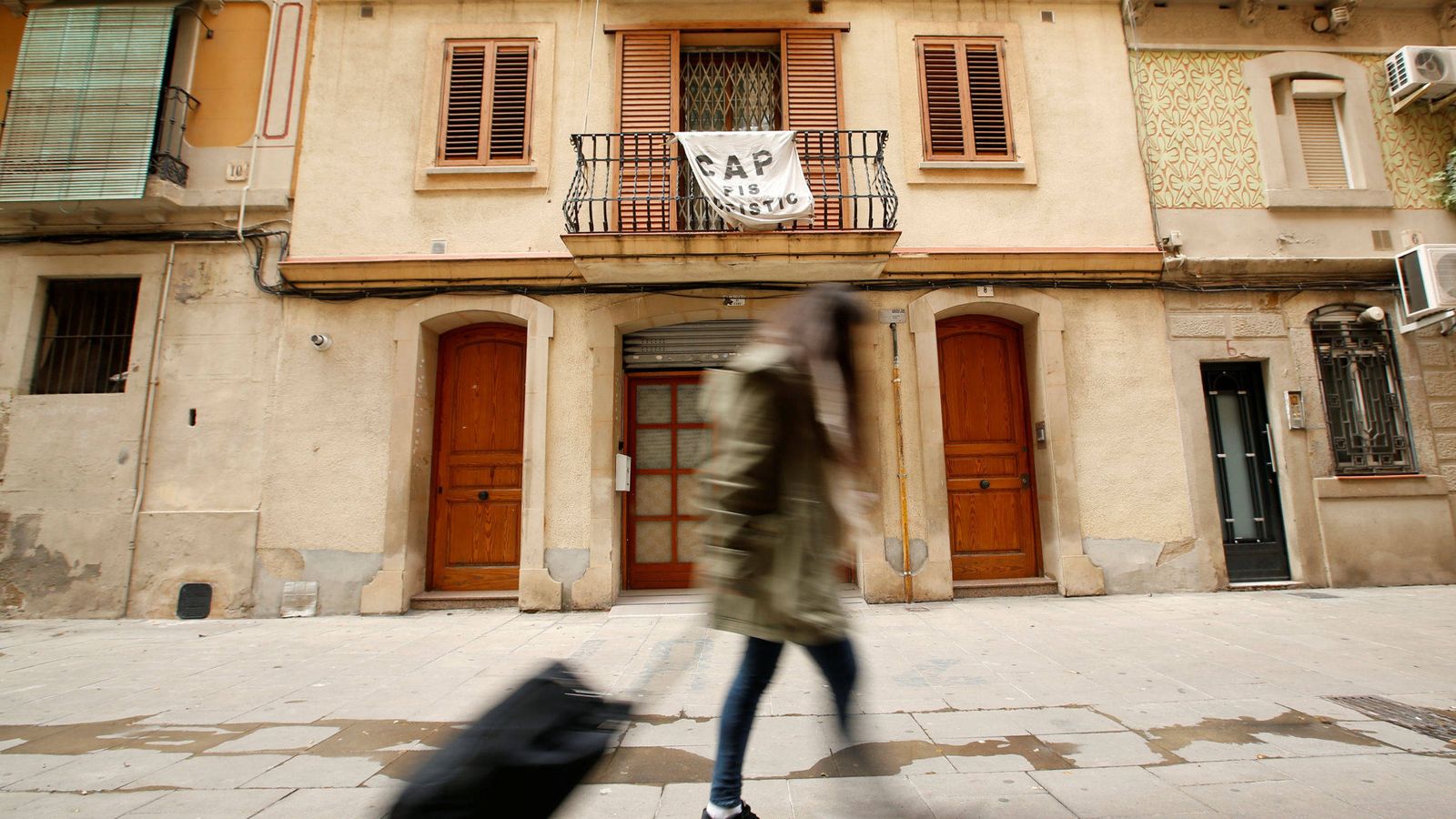 Foto: Una joven sostiene su maleta frente a una pancarta contra Airbnb. (Reuters)