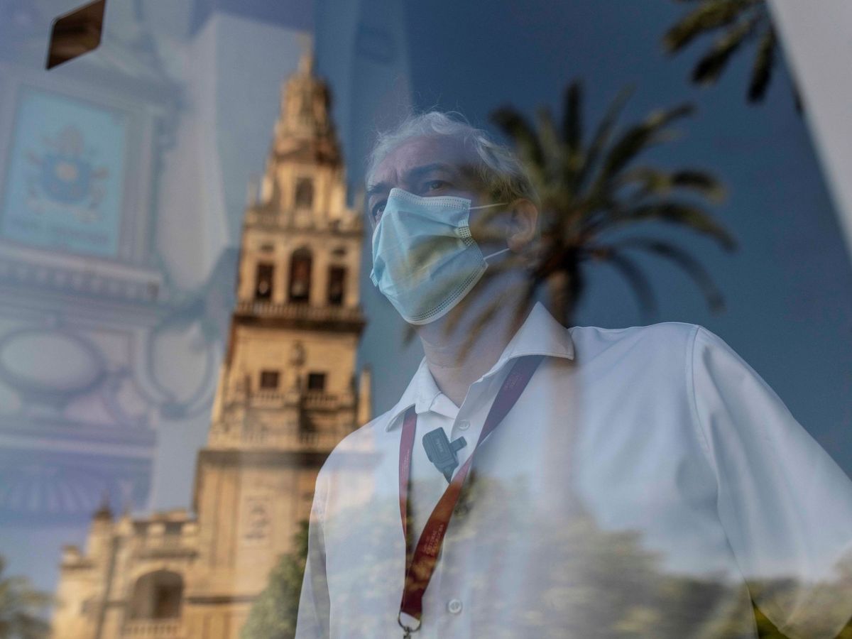 Foto: Un trabajador mira a través de una cristalera con la imagen reflejada de la Torre de la Mezquita-Catedral de Córdoba. (EFE)