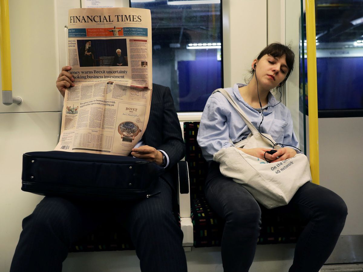 Foto: Una persona lee el Financial Times mientras una mujer duerme en un metro de Londres en 2017. (Reuters)