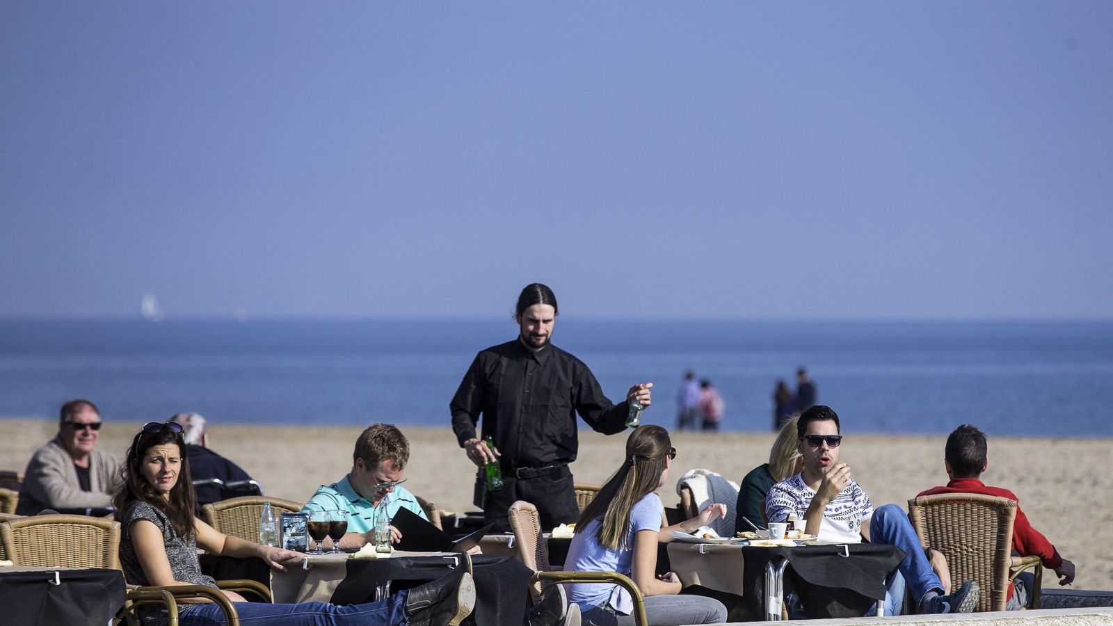 Foto: Varias personas disfrutan de las temperaturas suaves tomando un aperitivo en una terraza en la playa de La Malvarrosa de Valencia. (EFE)