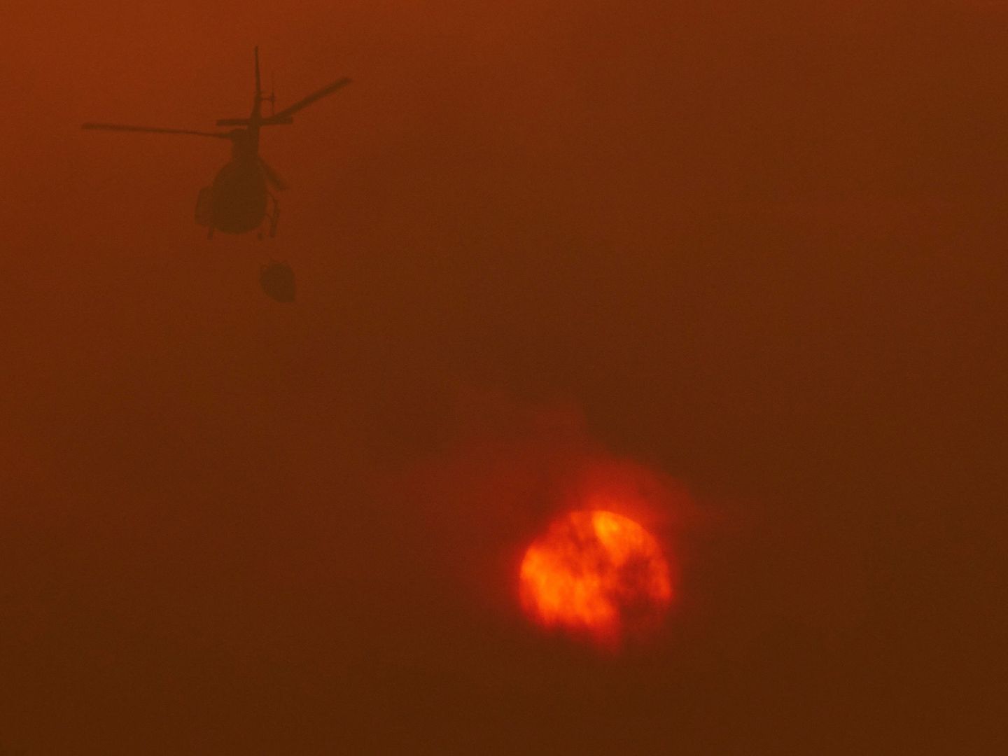 Un helicóptero de los servicios de extinción trabaja junto a las llamas. (EFE)