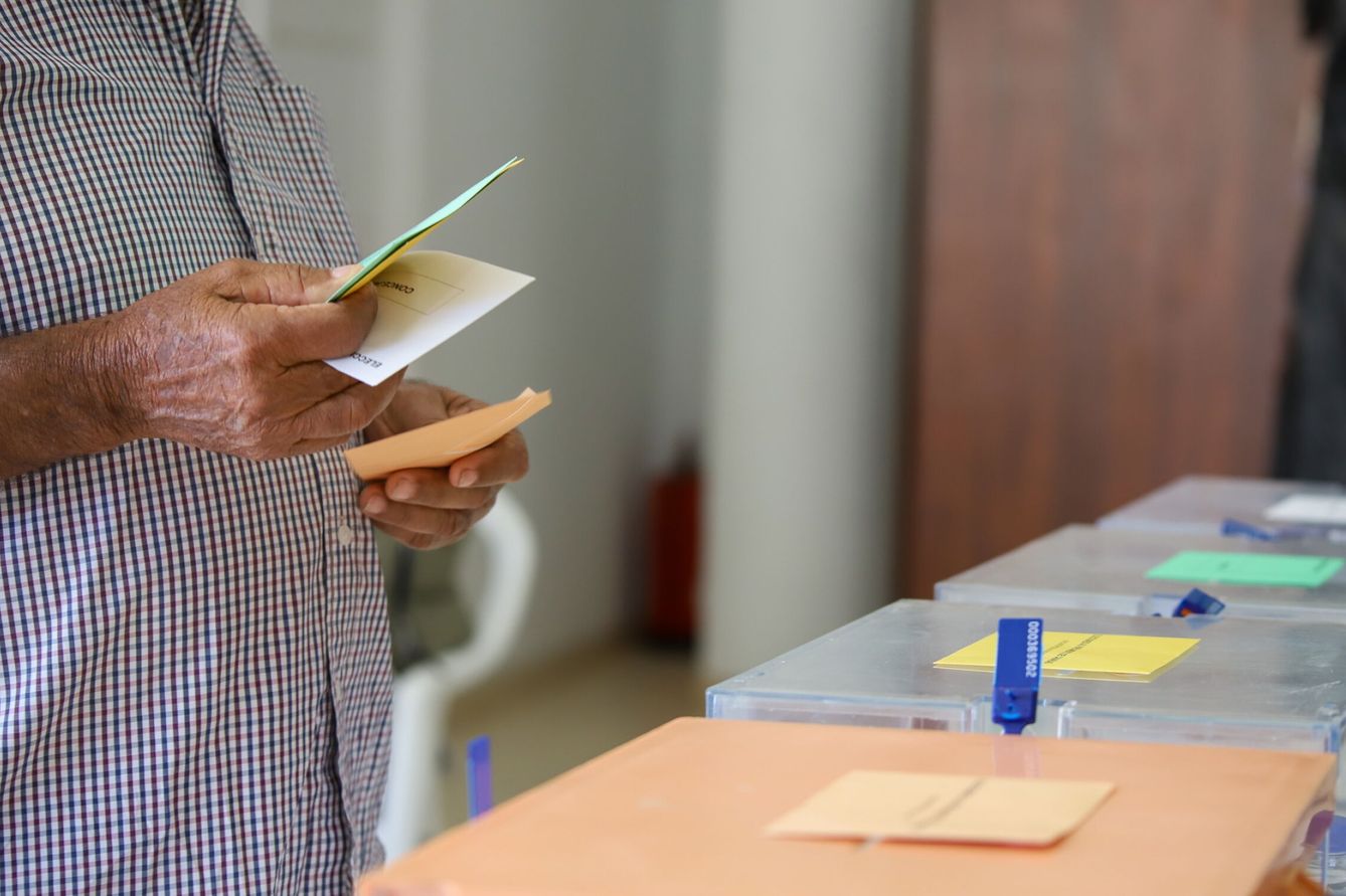 Un hombre sostiene sus papeletas de votación ante las urnas de la mesa en el colegio electoral. (EFE/Luis G. Morera)