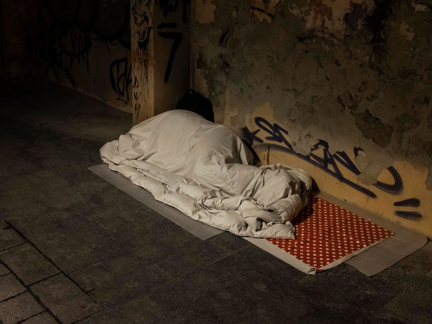 Una persona sin techo duerme tapada con un edredón en una calle de Valencia. (EFE)