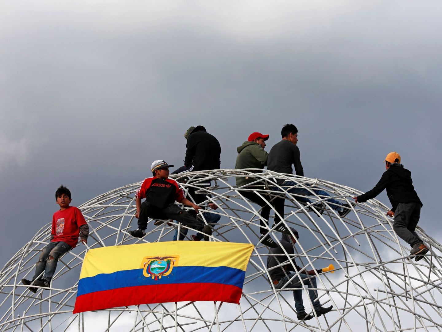 Varios manifestantes, durante el funeral de Tucumbi, sobre una estructura de hierro en Quito. (Reuters)