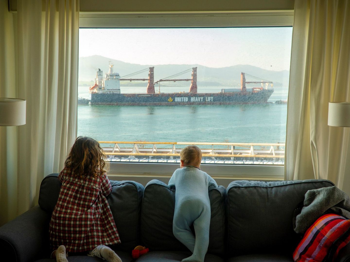 Dos niñas observan desde casa la entrada de barcos mercantes en la bahía de Santander, este miércoles. (EFE)