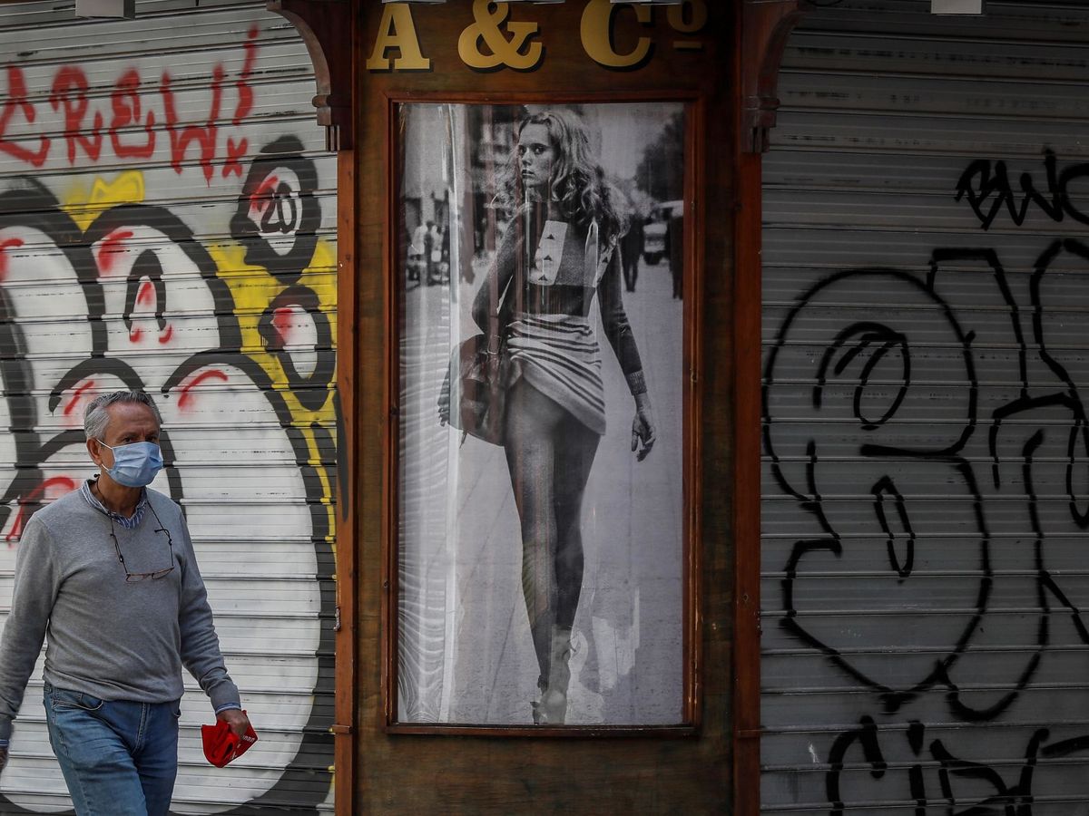 Foto: Un hombre camina junto a unas persianas de un bar cerrado. (EFE/José Manuel Vidal)