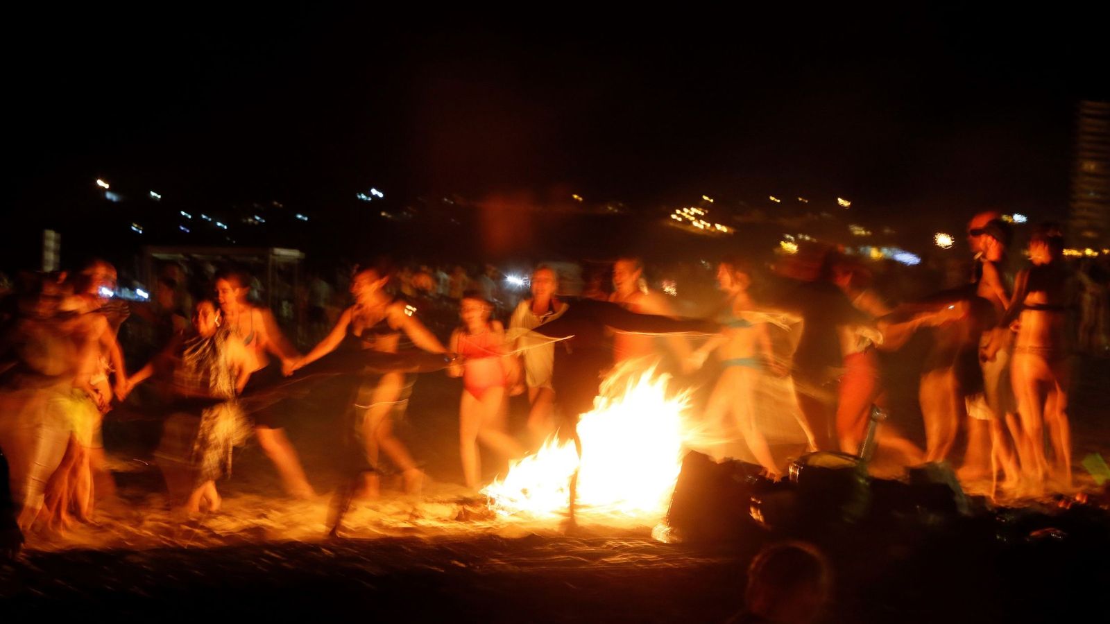 Foto: Un grupo de personas baila alrededor de una hoguera en la playa de San Juan de Alicante. (EFE)