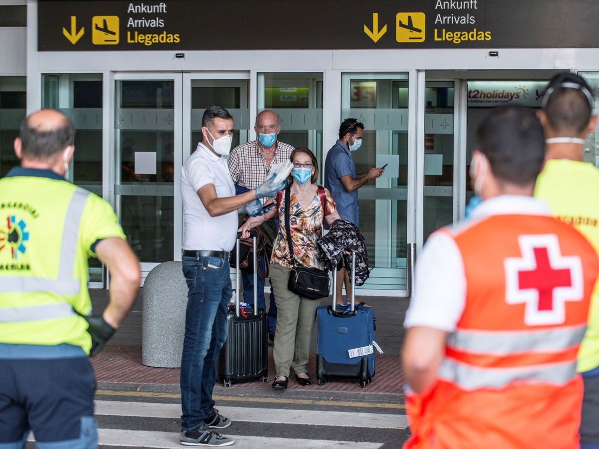 Foto: Dos viajeros reciben las indicaciones de los servicios de emergencias tras desembarcar en Lanzarote. (EFE)
