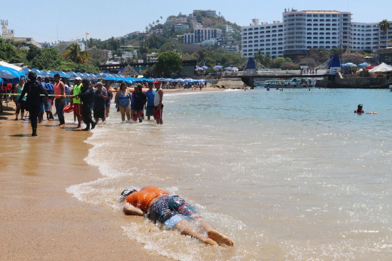 Un grupo de turistas y residentes mira el cadáver de una víctima de un ajuste de cuentas relacionado con el narcotráfico en Acapulco, en abril de 2018. (Reuters)