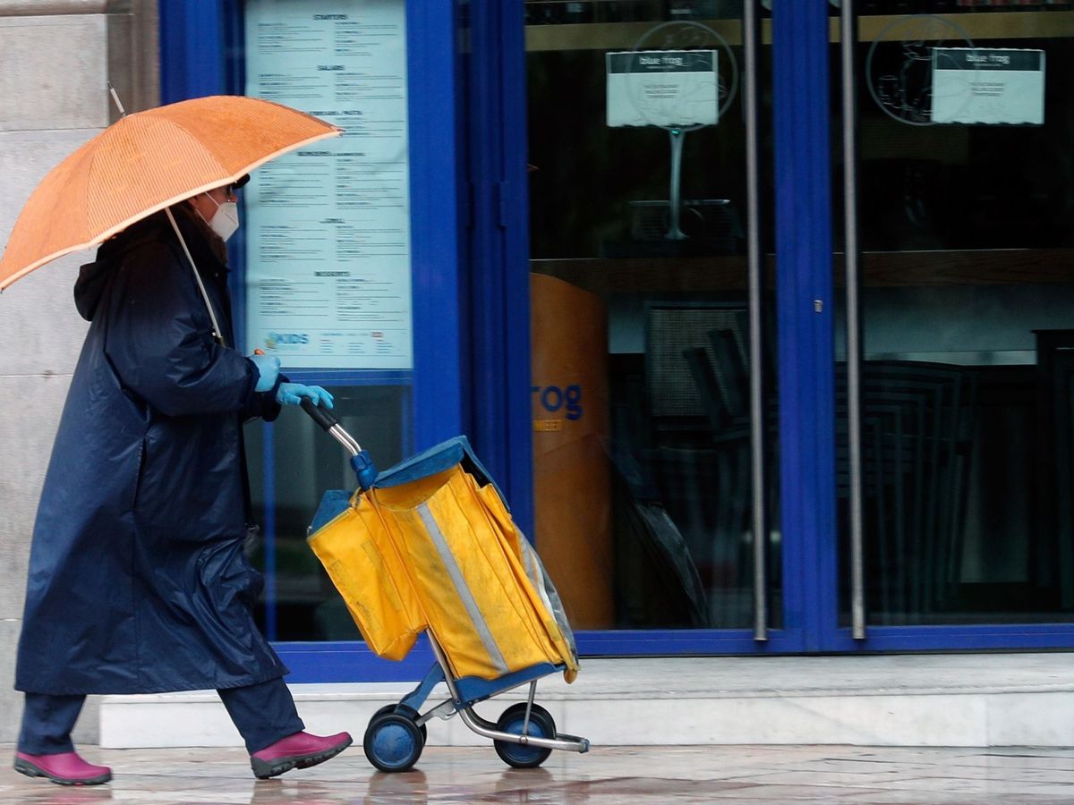 Foto: Una cartera, protegida con mascarilla, reparte el correo bajo la lluvia. (Kai Försterling/EFE)