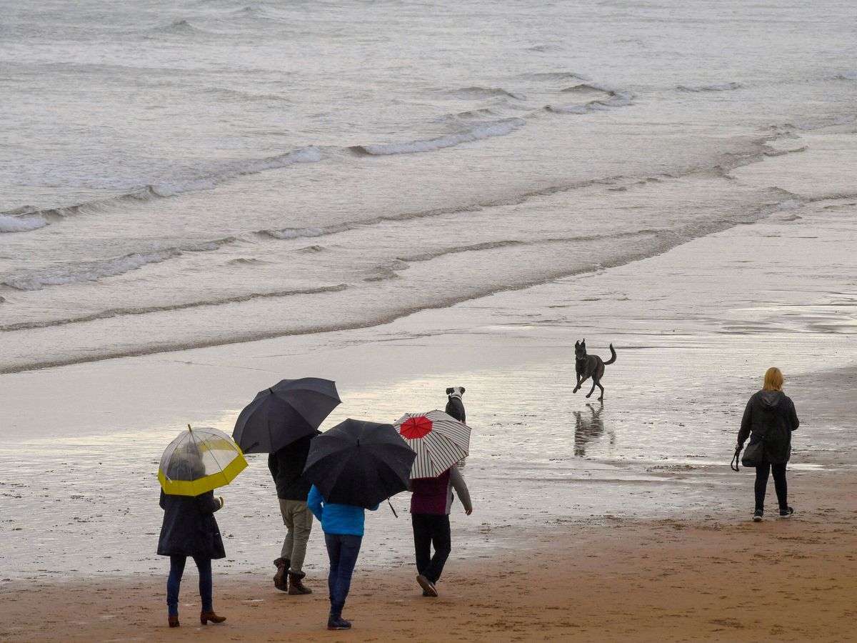 Foto: Unas personas pasean con paraguas en una playa en Gijón. (EFE/Eloy Alonso)
