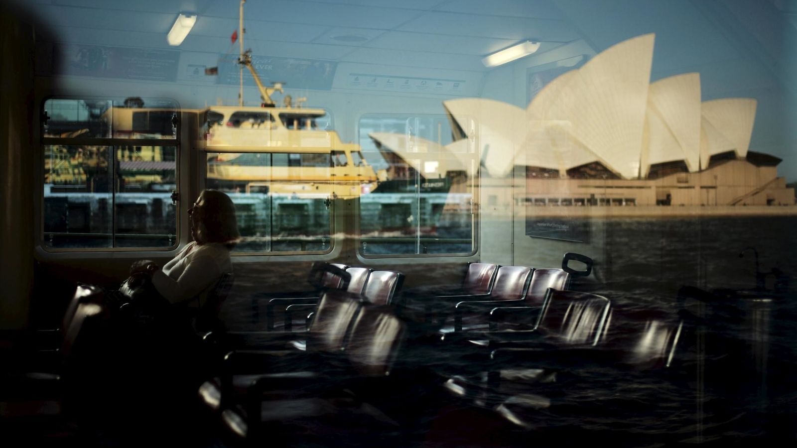 Foto: Una pasajera en un ferri, cuyo cristal refleja la Casa de la Ópera de Sídney. (Reuters)