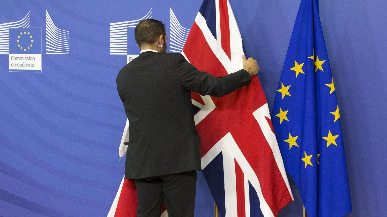 Foto: Un empleado de la Comisión Europea coloca una bandera británica junto a otra de la UE antes de la reunión de Cameron y Juncker en Bruselas (Reuters). 
