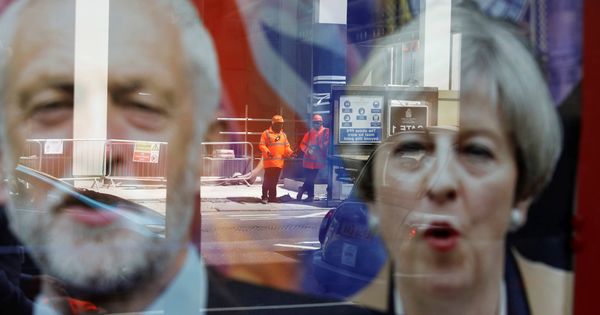 Foto: Trabajadores reflejados en una ventana con las imágenes de Jeremy Corbyn y Theresa May, en Londres. (Reuters) 