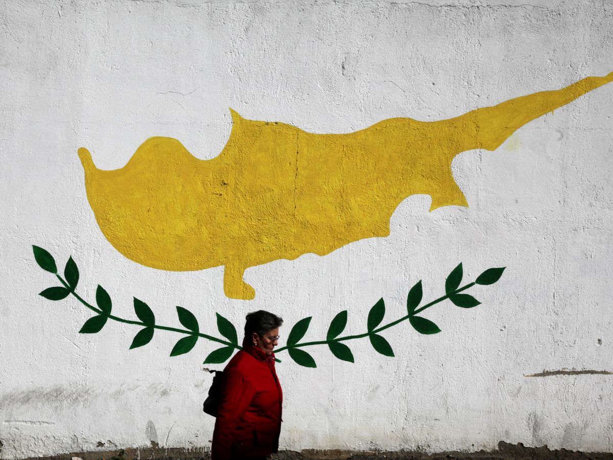 Foto: Una mujer camina frente a un mural con la bandera de Chipre. (Reuters)