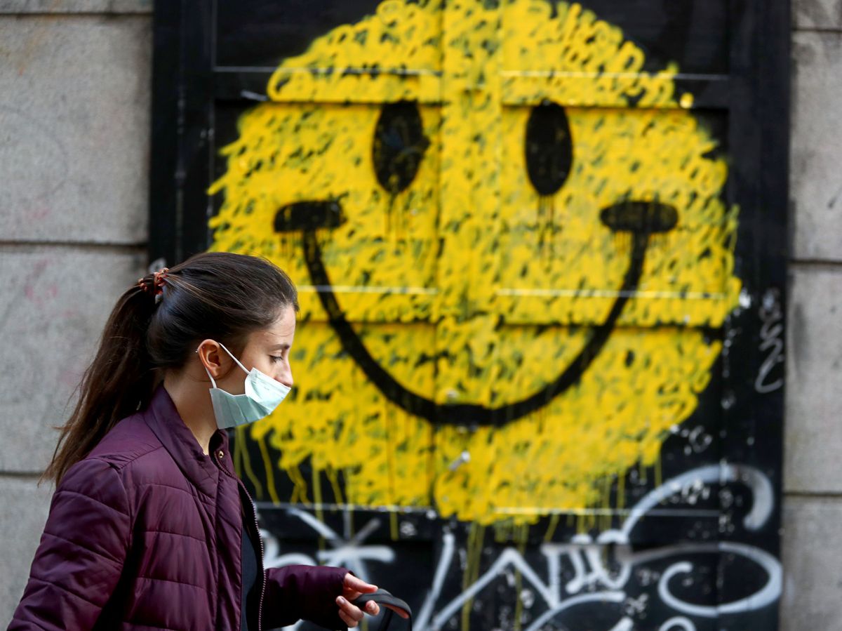 Foto: Una mujer, ataviada con mascarilla, pasea frente al portal de una tienda con una cara sonriente pintada. (Reuters)