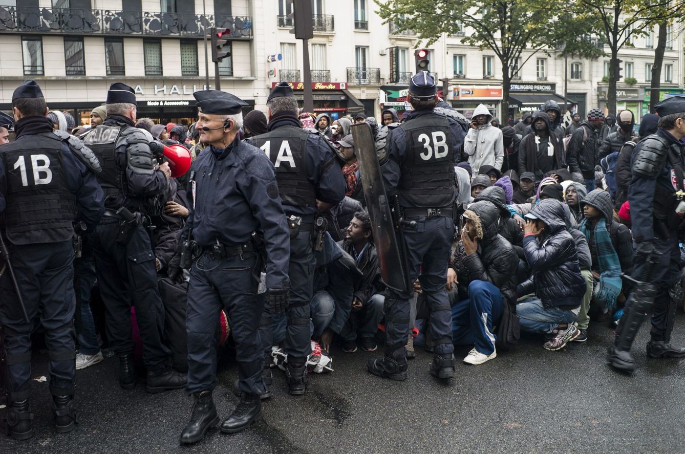 Agentes de policía galos permanecen en guardia mientras agrupan a varios inmigrantes durante desalojo de un campamento en el distrito 19 de París. (EFE)