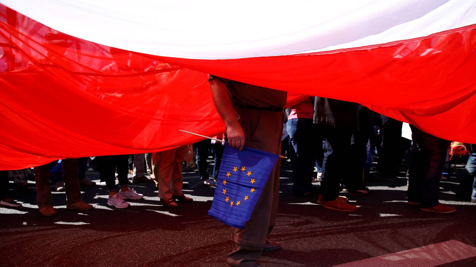 Foto: Un hombre sostiene una bandera de la UE junto a una enorme bandera polaca durante una protesta en Varsovia (Reuters).