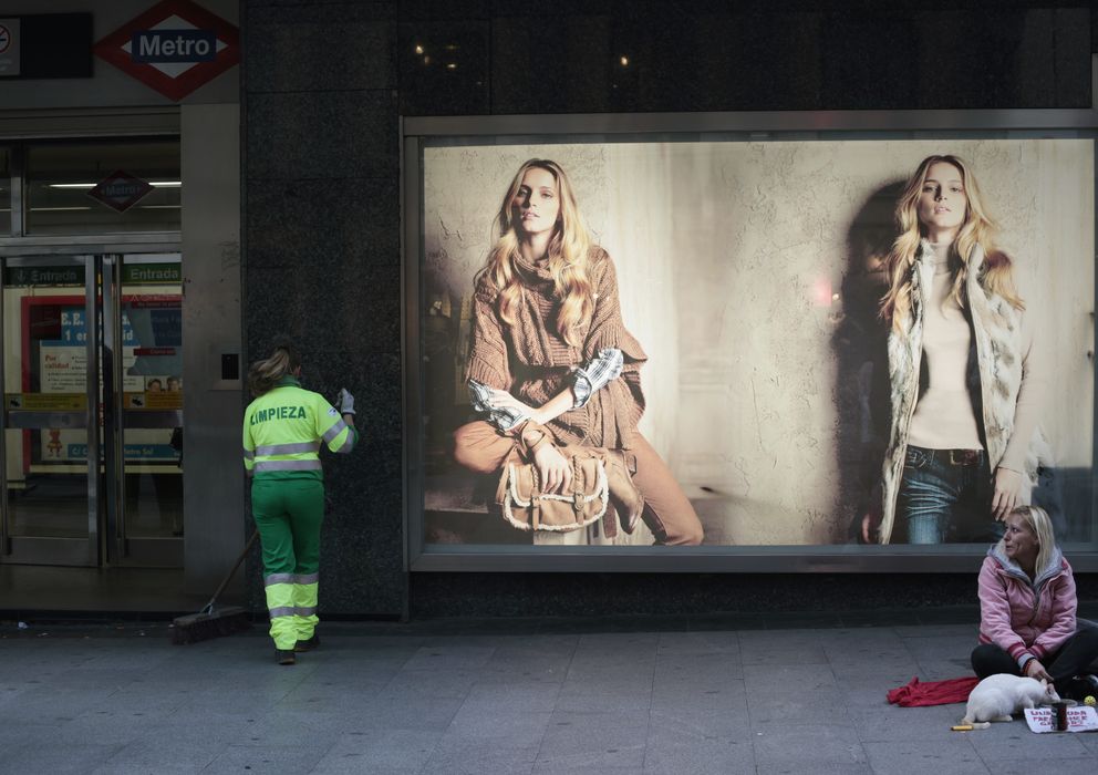 Foto: Una mujer pide limosna y otra barre la calle junto a unos grandes almacenes en Madrid (Reuters)