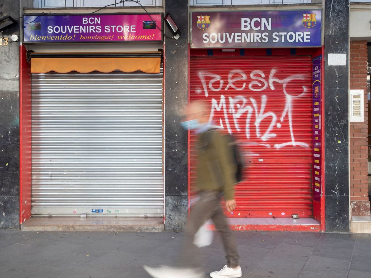 Foto: Un vecino pasa ante una tienda de recuerdos con la persiana bajada en Barcelona. (EFE)
