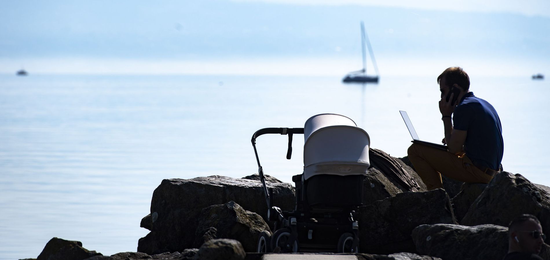 Un padre trabaja en su portátil y habla por teléfono junto al carrito de su bebé. (EFE)