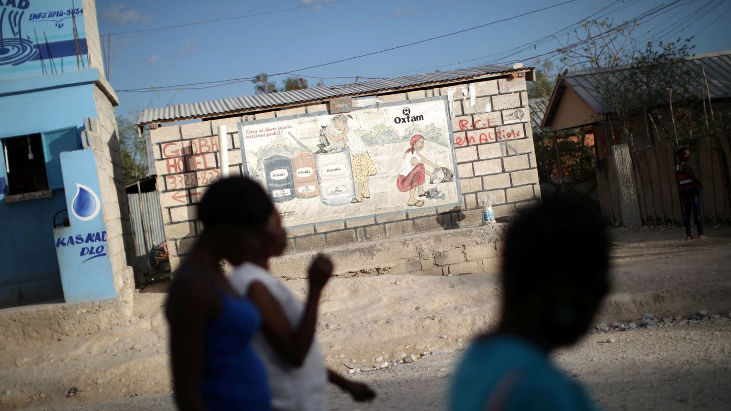 Mujeres pasan junto a un cartel de Oxfam en Corail, un campo de desplazados del terremoto de 2010, en las afueras de Puerto Príncipe (Reuters)