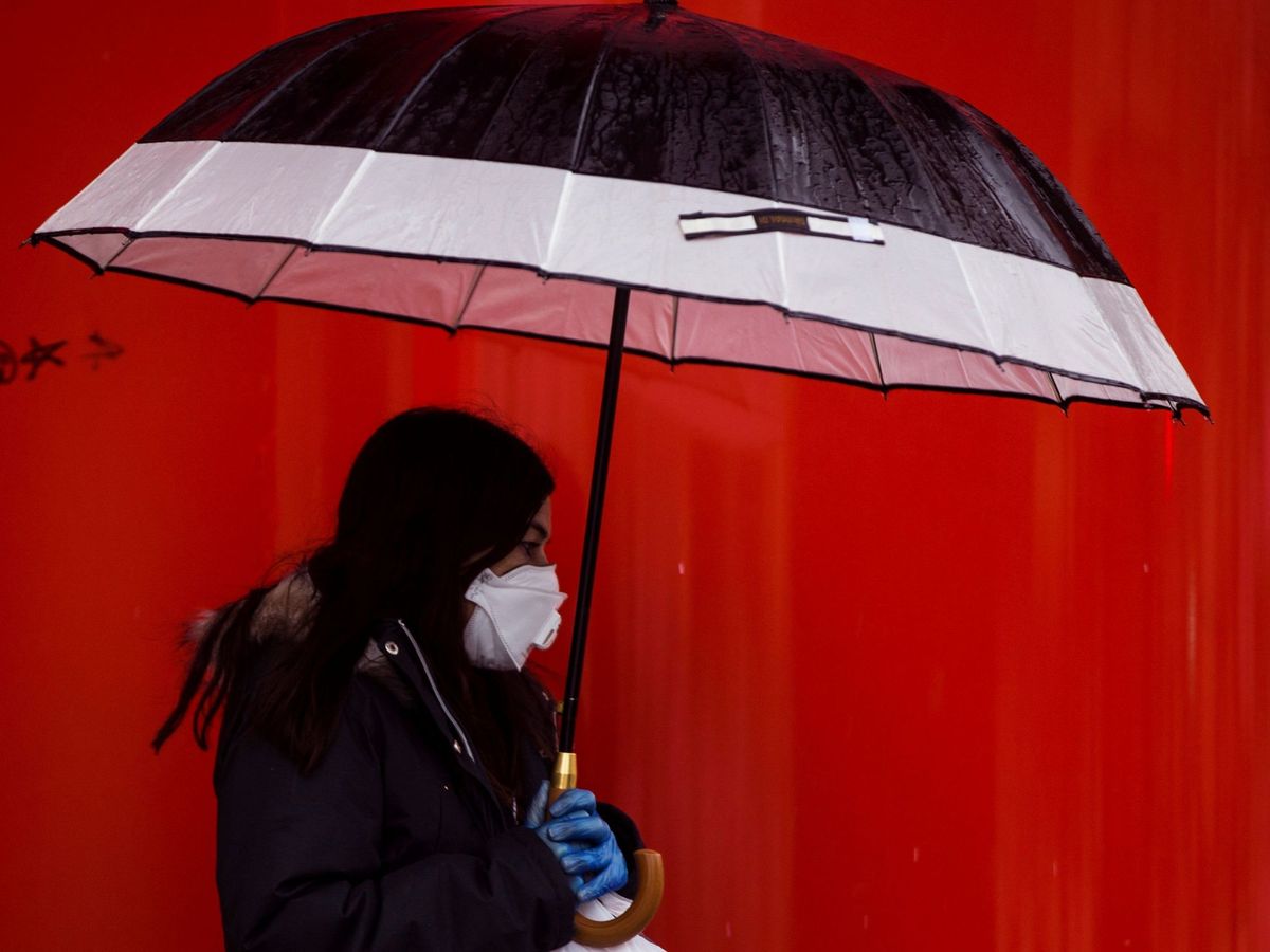 Foto: Una mujer camina bajo la lluvia con mascarilla y guantes en Málaga. (EFE)