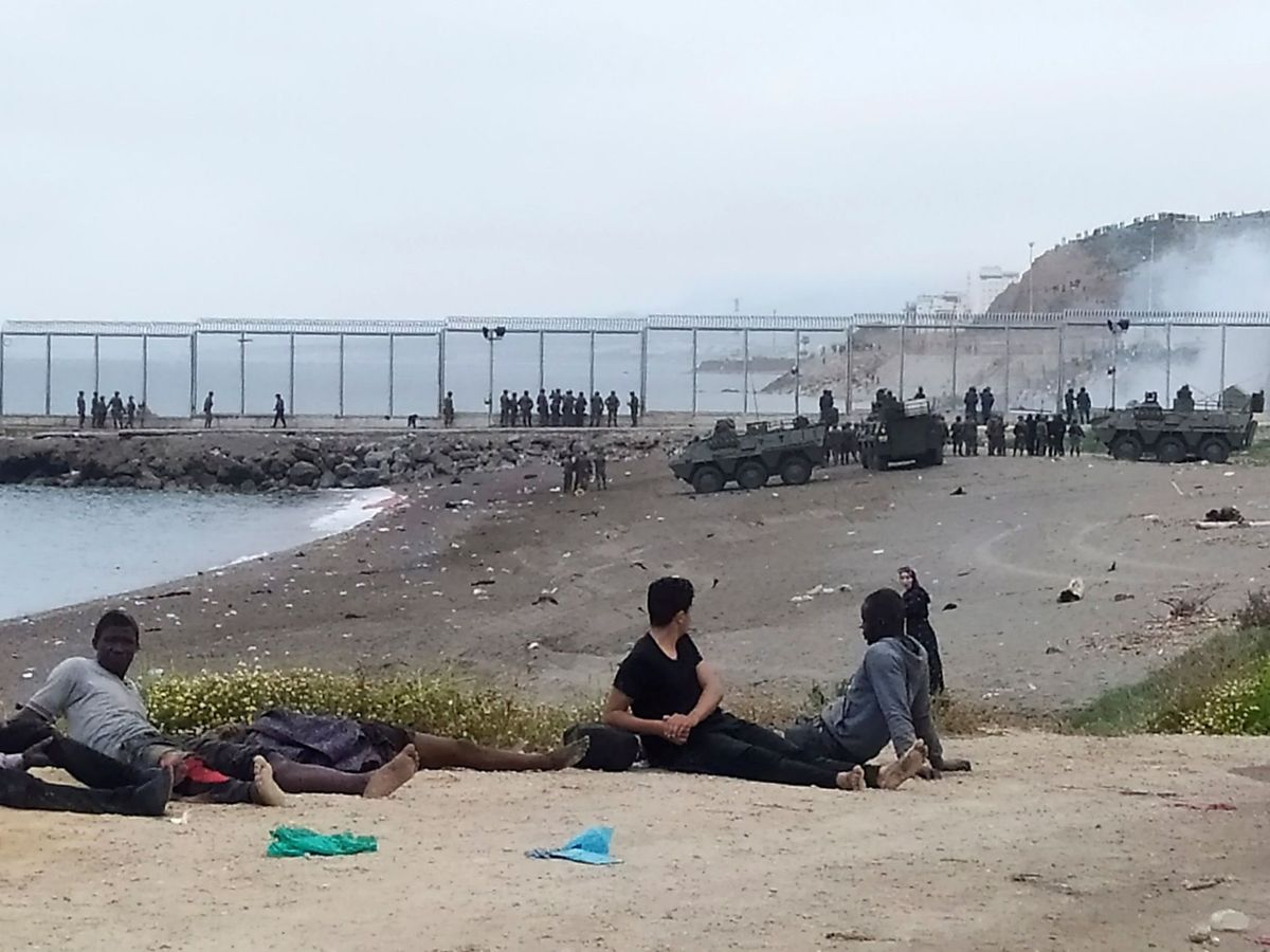 Foto: Un grupo de inmigrantes marroquí observa el despliegue del Ejército de Tierra en uno de los espigones fronterizos de Ceuta. (EFE)