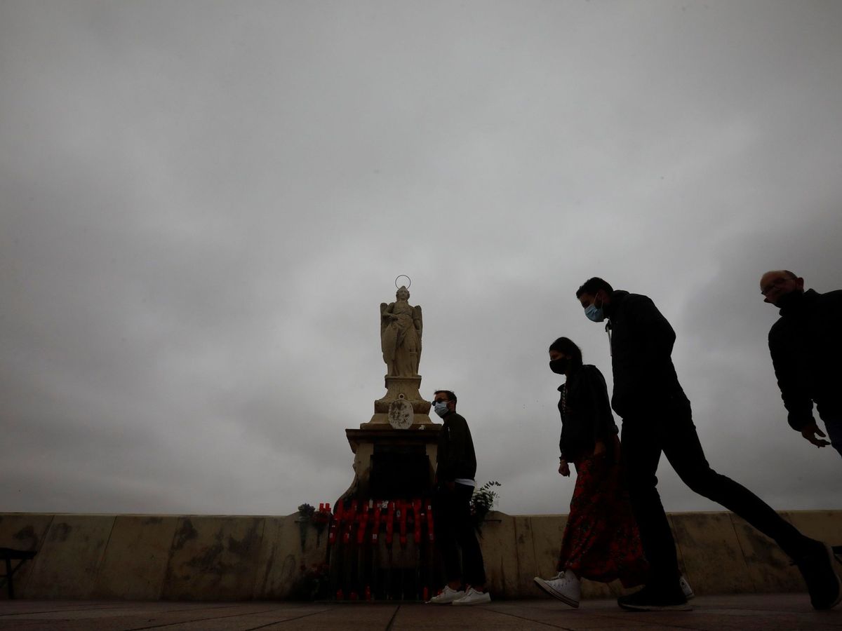 Foto: Varias personas pasan junto a la estatua del arcangel San Rafael situada en el puente Romano de Córdoba. (EFE)