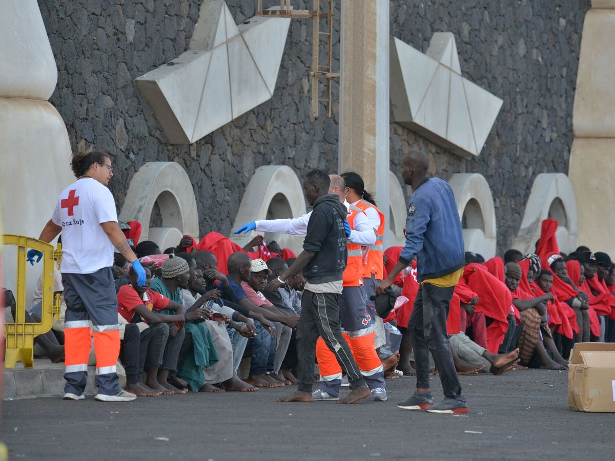 Foto: Trabajadores de la Cruz Roja al lado de los migrantes que han llegado en un cayuco al puerto de La Restinga. (Europa Press)