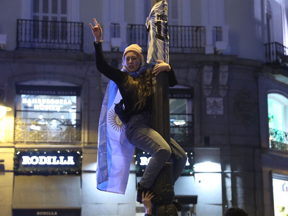 Foto: Una mujer argentina, en una farola de la Puerta del Sol celebrando la victoria de su país en el Mundial de Qatar. (Reuters/Isabel Infantes)