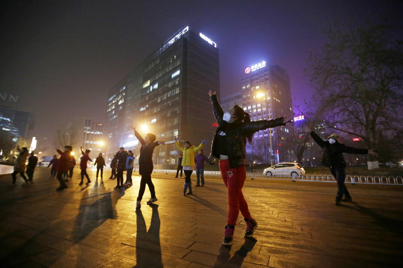 Mujeres con mascarillas bailan entre la niebla de la contaminación, en Pekín. (Reuters)