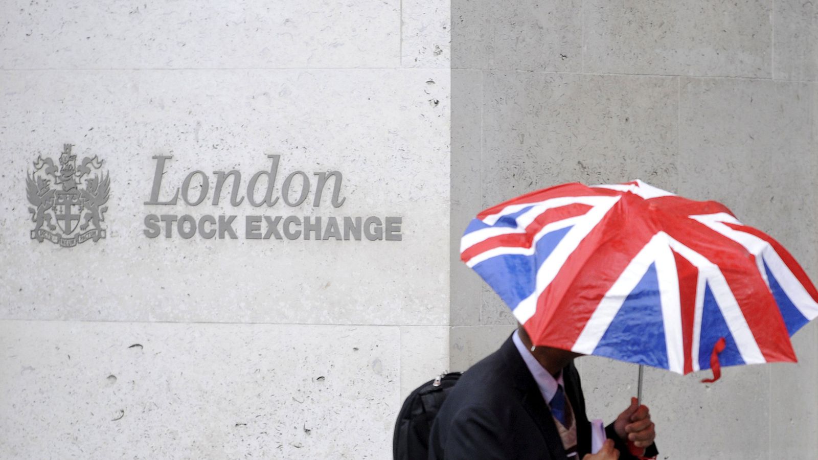 Foto: Un hombre se cubre de la lluvia a su paso por la Bolsa de Londres. (Reuters)
