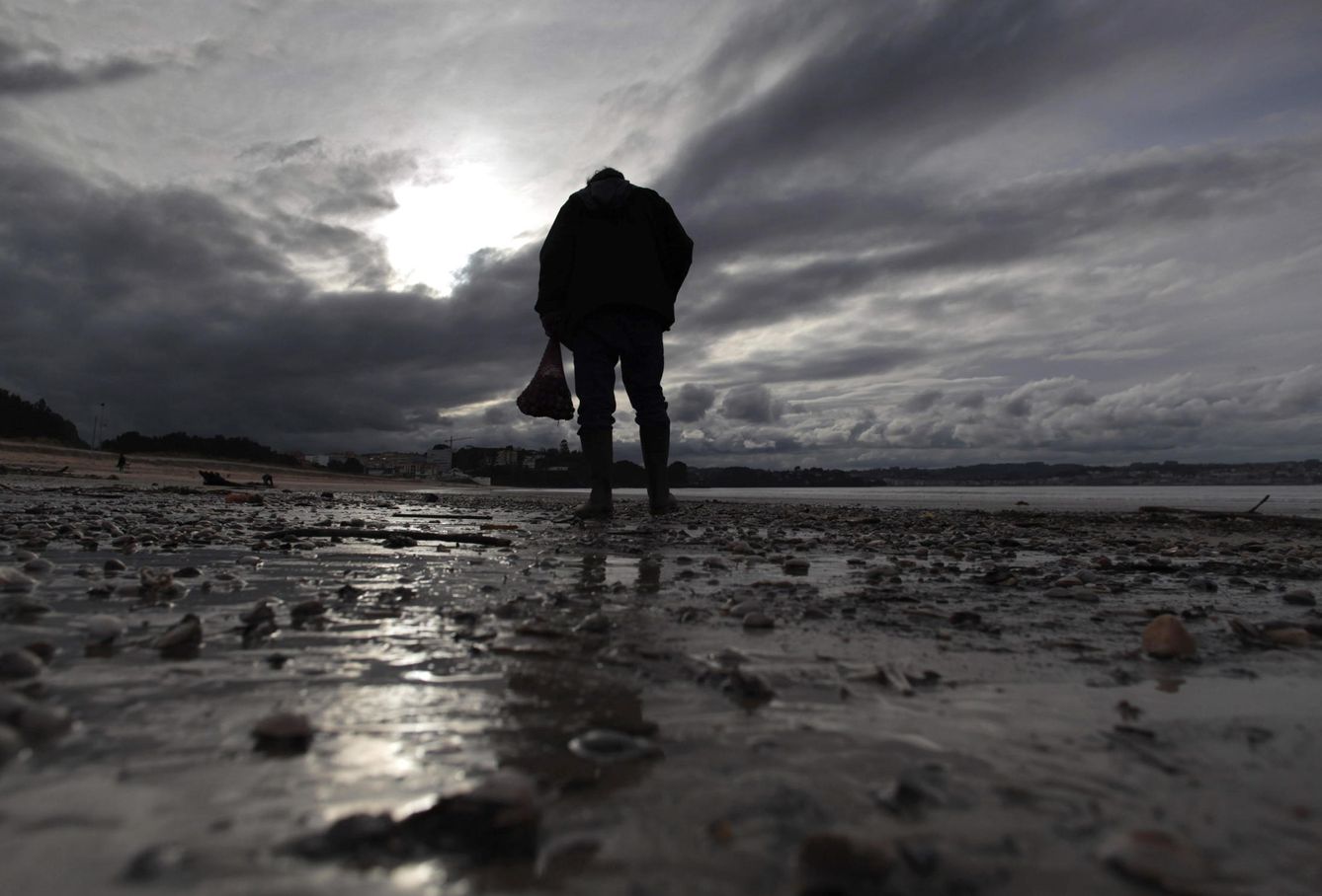 Un hombre recoge almejas en la orilla de la playa Grande de Miño, en A Coruña. (EFE/Cabalar)