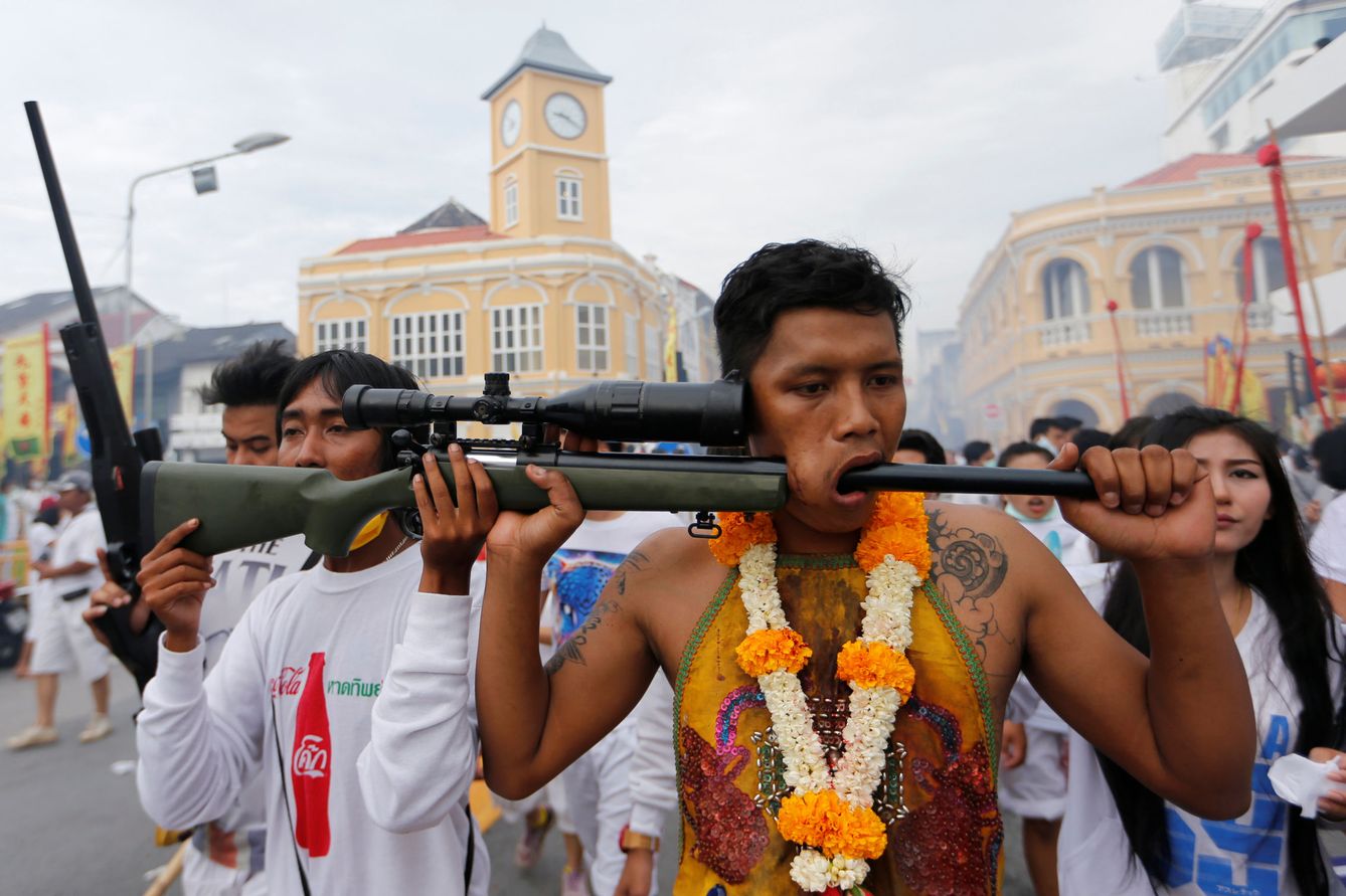 Un deboto de un santuario utiliza un arma para mostrar su mejilla perforada durante un festival en Tailandia. (Reuters)