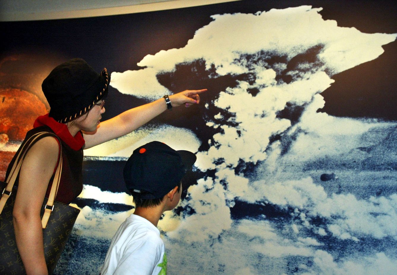 Una madre y su hijo miran una fotografia con la nube que desencadenó el lanzamiento de la bomba atómica en Hiroshima. EFE