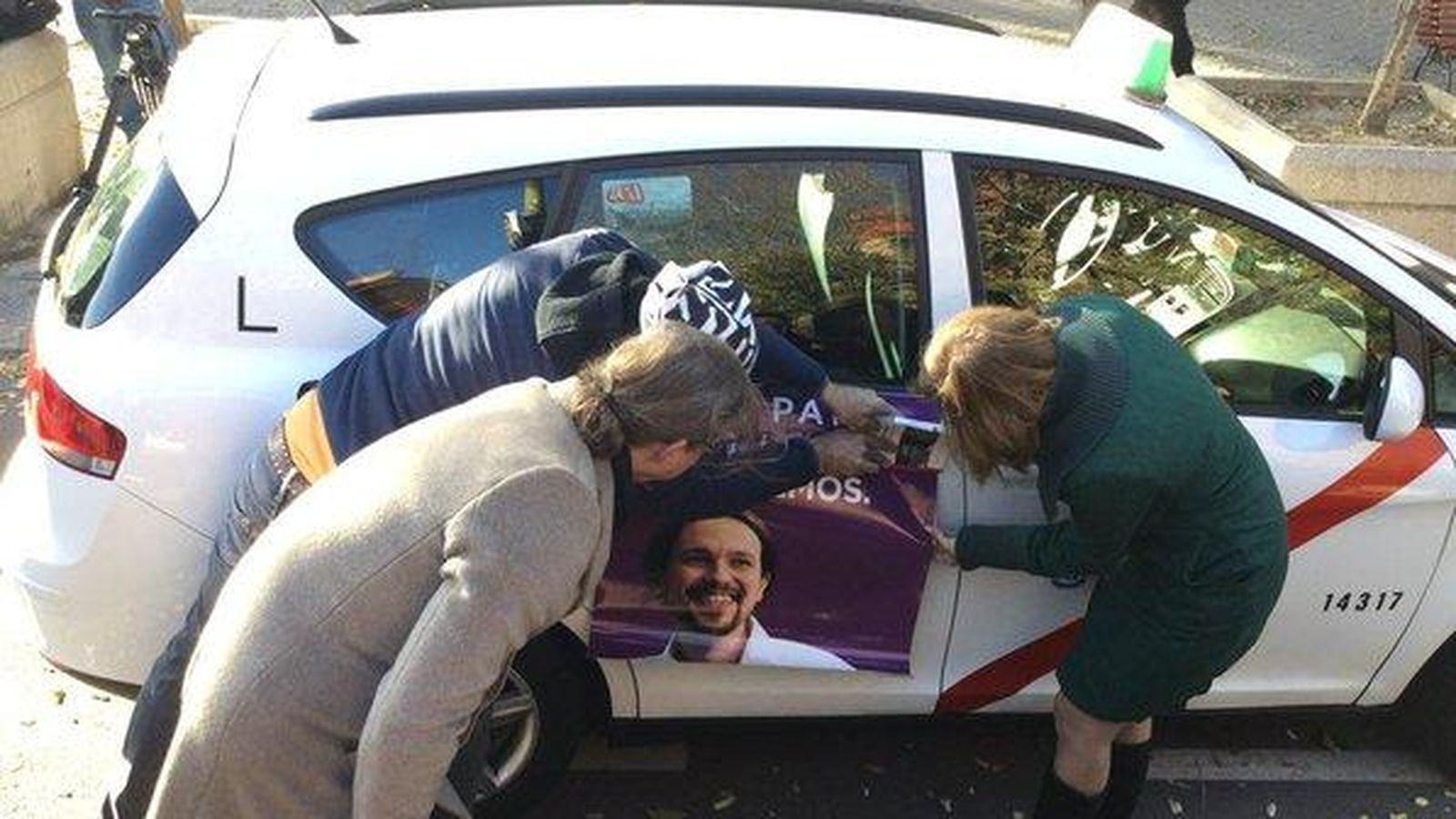 Foto: Un taxista pega un cartel electoral de Podemos en la puerta de su vehículo. (Twitter) 