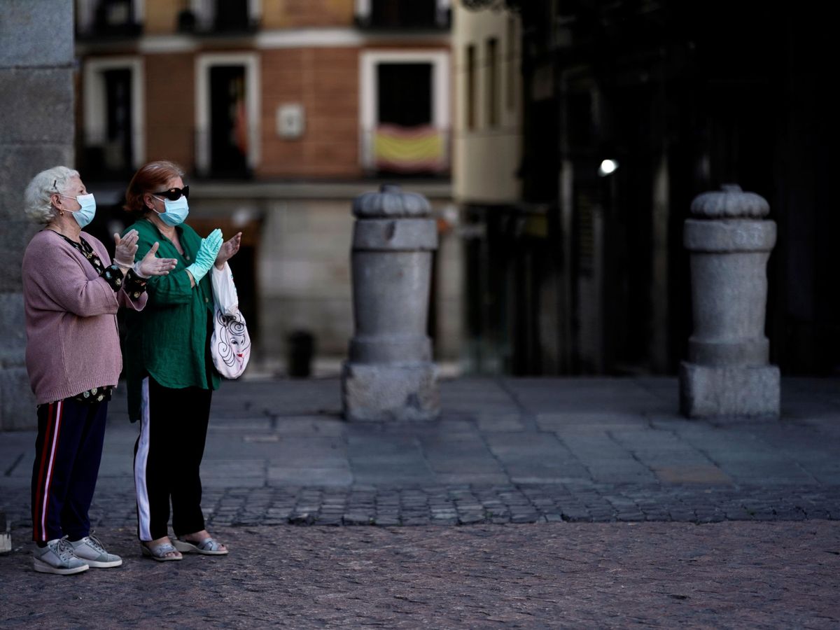 Foto: Dos ancianas con mascarillas aplauden en la Plaza Mayor de Madrid. (Reuters)