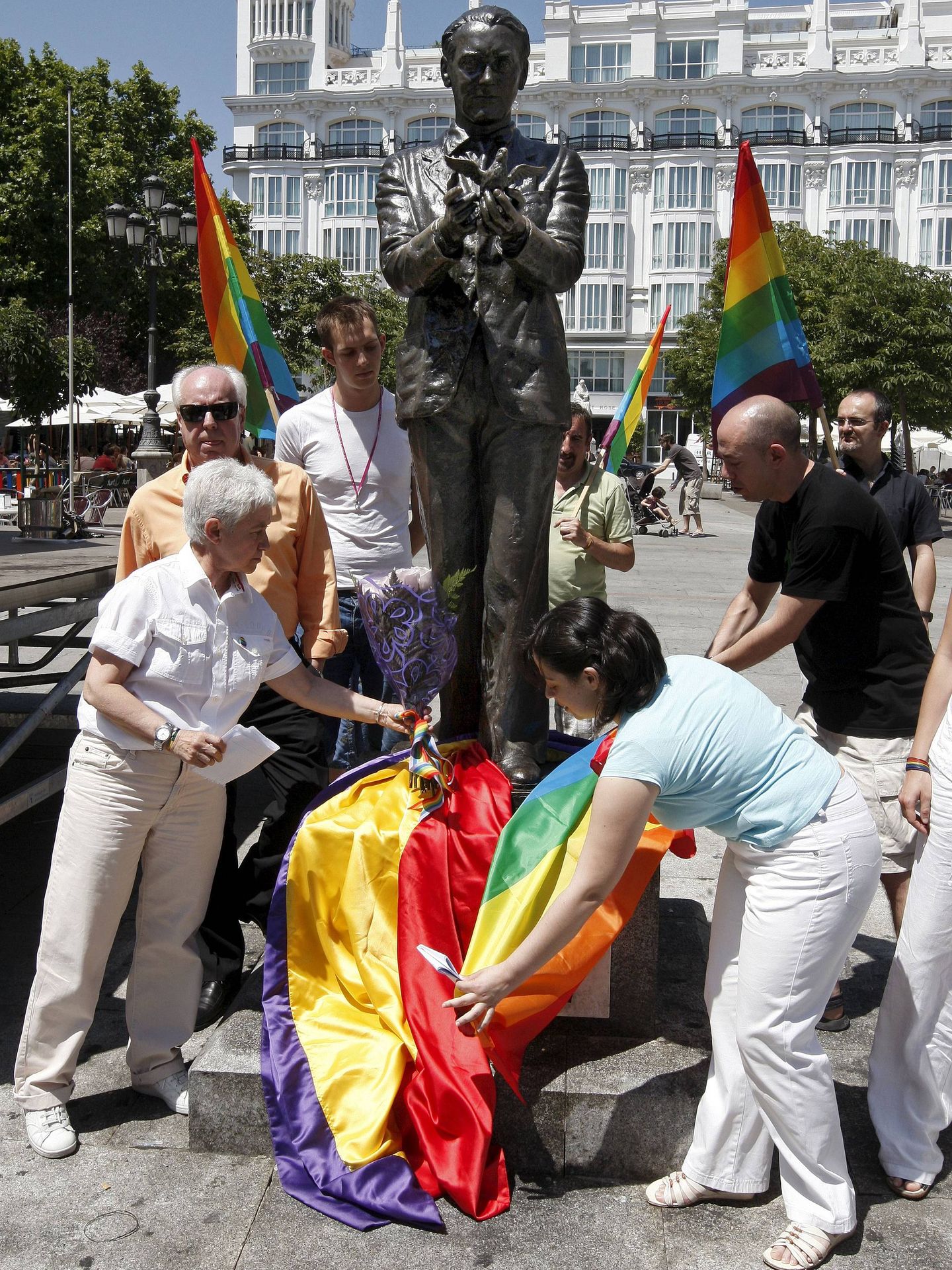 Boti García (iz) y Arancha Fernández (d) junto a Eduardo Mendicutti, detrás con gafas, colocan un ramo de flores y una bandera en la estatua  de Lorca en Madrid en 2009. EFE/Bernardo Rodríguez.