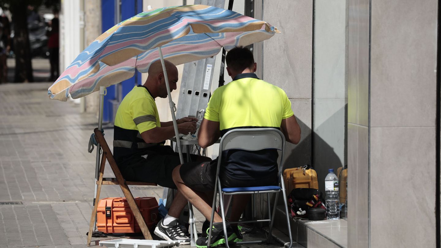 Dos operarios de telefonía se protegen con una sombrilla del intenso sol y calor. (EFE)
