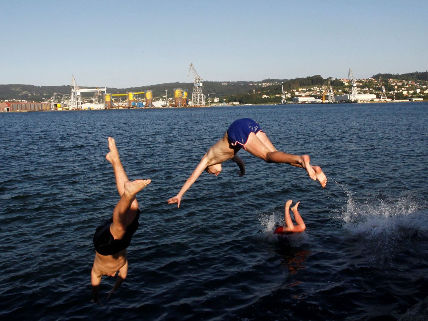 Unos jóvenes saltan al agua en la playa del barrio de Carranza en Ferrol, A Coruña (EFE)