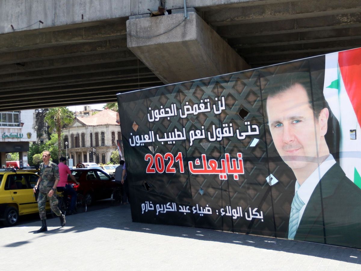 Foto: Varios peatones pasa junto a un cartel electoral que muestra al presidente sirio, Bachar Al Assad. (EFE) 