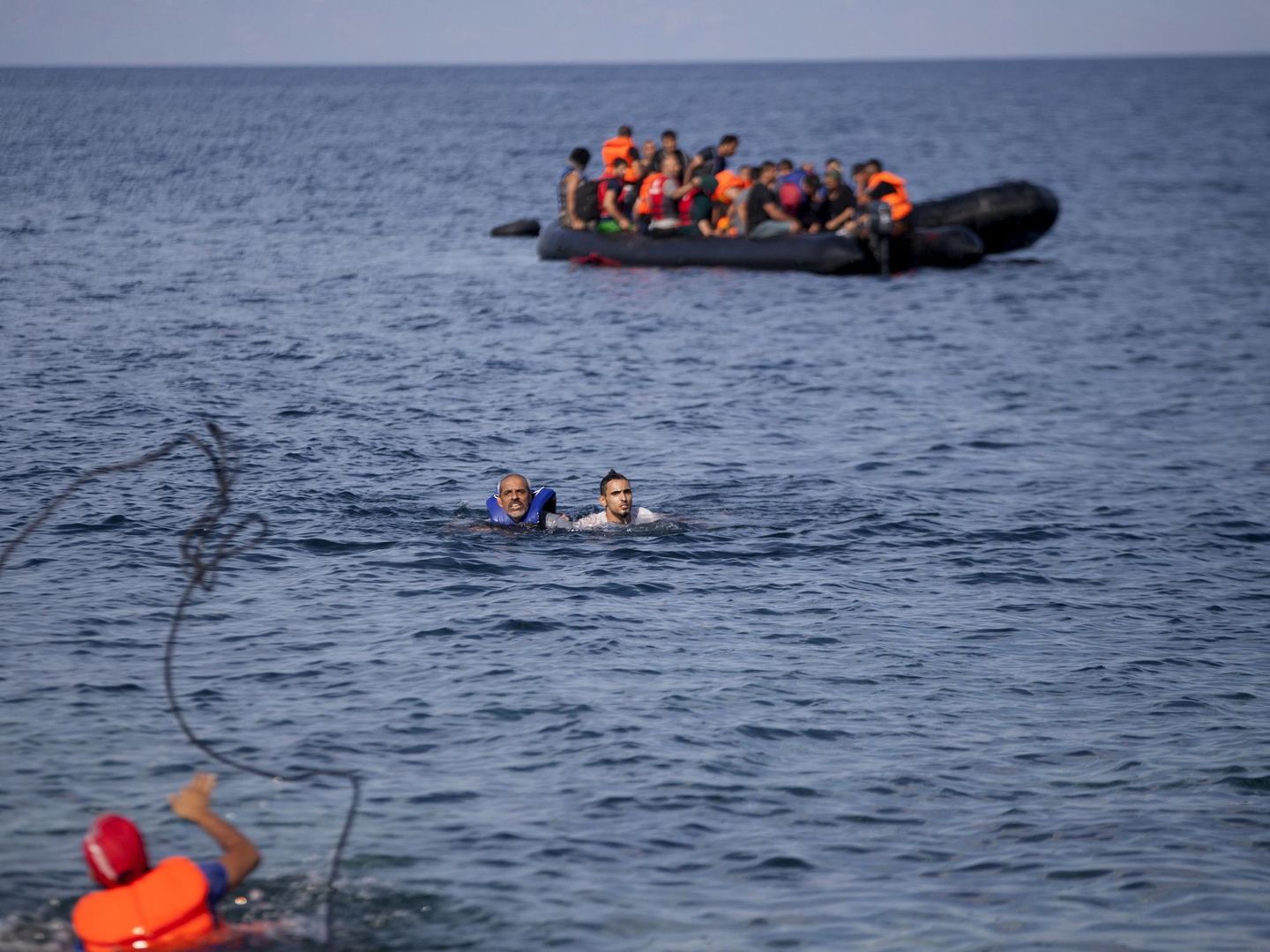 Un hombre arroja una cuerda a unos refugiados sirios que abandonaron una barca que se hundía frente a Lesbos (Reuters).