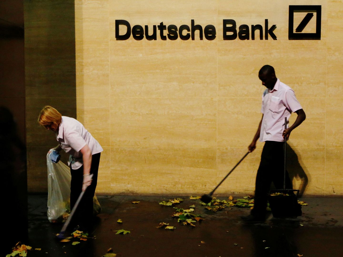 Dos trabajadores barren hojas fuera de las oficinas del Deutsche Bank en Londres. (Reuters)