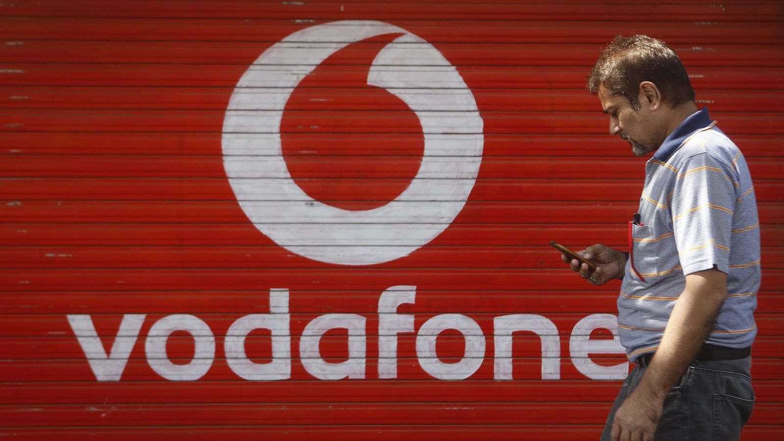Foto: Un hombre comprueba el móvil delante de una tienda de Vodafone. (Reuters)