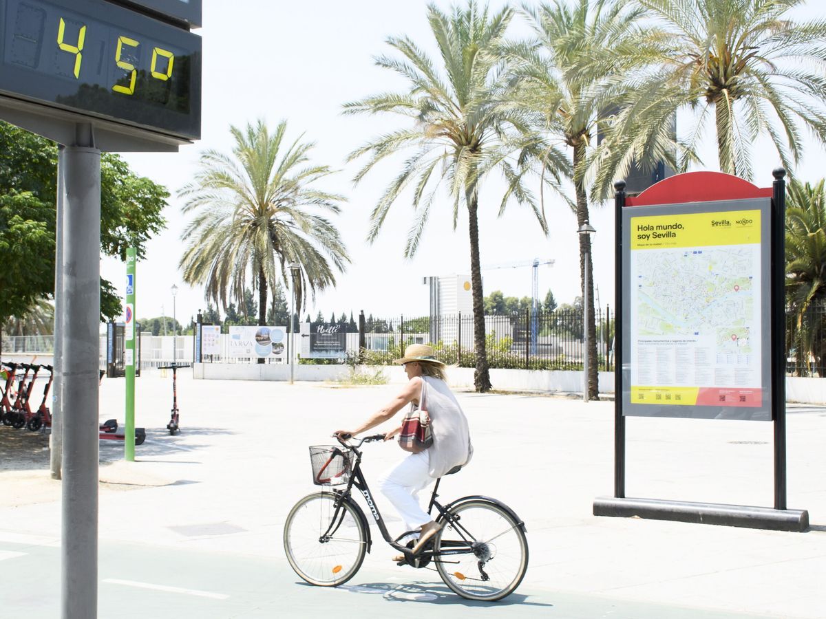 Foto: Una mujer pasea en bicicleta junto a un termómetro a 45 grados en Sevilla. (EFE/Raúl Caro)